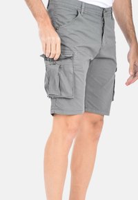 Pantaloni cargo grigi con zip frontale, numerose tasche laterali e vestibilità rilassata. Realizzati in tessuto leggero con una consistenza liscia.
