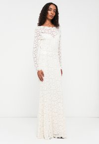 Dolga bela čipkasta obleka z dolgimi rokavi, cvetlični vzorec, prilegajoč se korzet in razporek. Teksturna čipka daje globino oblikovanju.