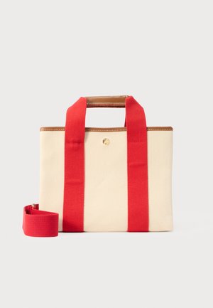 Μπεζ ορθογώνια τσάντα καμβά με φαρδιές κόκκινες λουρίδες, καφέ δερμάτινη επένδυση και αποσπώμενο κόκκινο λουρί ώμου σε ανοιχτό φόντο.