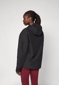 Wasserabweisende schwarze Jacke mit Kapuze, die eine lockere Passform, lange Ärmel und elastische Bündchen aufweist. Das Material wirkt glatt und leicht.