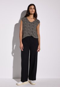 Top de patrones en blanco y negro con mangas cortas, combinado con pantalones anchos negros y zapatillas blancas sobre un fondo claro.