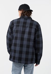 Checkered flannel shirt in dark blue and black, featuring a button-up collar, long sleeves, and a loose fit. Notable texture appears soft.