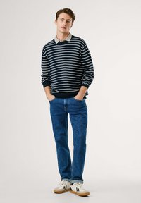 Jūras spēku svītrots džemperis ar bežīgu apkakli, zili džinsi un baltas kedas ar melniem un sarkaniem akcentiem. Tekstūrēts adījums un brīvajā stilā.