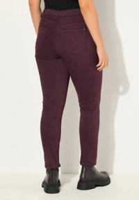 Burgundské skinny kalhoty s elastickým pasem, dvěma zadními kapsami a hladkým povrchem, spárované s robustními černými kotníkovými botami.
