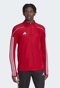 Pullover atletico rosso con mezza zip, dotato di dettagli texturizzati sulle spalle, strisce bianche sulle maniche e logo Adidas sul petto.