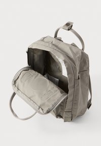 Grå tygryggsäck med justerbara remmar, rund form och ett zip-försett huvudfack. Inuti har den ett litet, vadderat fack.