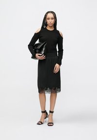 Czarna bluzka z odkrytymi ramionami, dopasowanym gorsetem i spódnicą wykończoną koronką. Połączona z czarnymi sandałami na wysokim obcasie i skórzaną torebką.