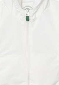 Giacca in nylon bianca con zip frontale, tirante verde e cappuccio. Presenta una texture liscia e un'etichetta rotonda del marchio all'interno.