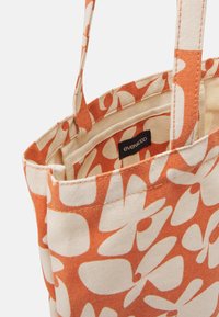 Sac tote en toile avec motif floral blanc abstrait sur fond orange et étiquette de marque « even&odd » à l'intérieur.