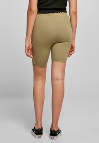 Beige stretchshorts met een strakke pasvorm, die net boven de knieën eindigen, met een kantaccent aan de zijkant. Draagt met zwarte sneakers.