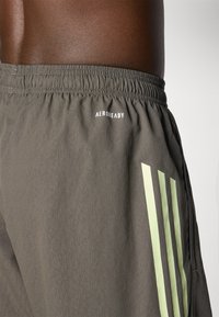 Mørkegrå shorts med elastisk talje, der har en hvid "AEROREADY" logo og tre lodrette lysegrønne striber på siden. Glat tekstur.