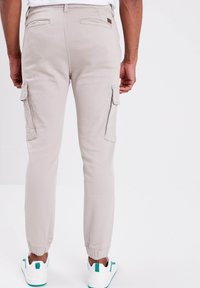 Lichtbeige cargobroek met twee zijzakken, taps toelopende enkelboorden en een zachte katoenstructuur, gecombineerd met witte sneakers met groene accenten.