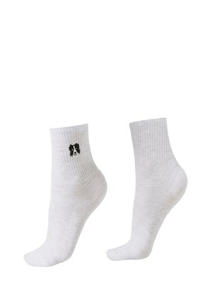 Witte geribbelde enkelsokken met een klein zwart-wit hondengezicht borduursel aan de buitenkant van één sok.