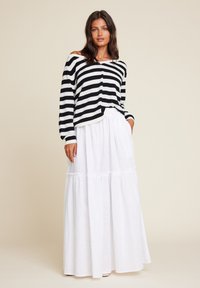 Svart og hvitstripet langermet topp paret med en flytende hvit maxiskjørt med volanger og et avslappet design.