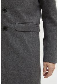 Manteau en laine gris foncé avec un design ajusté, fermeture par boutons et un élégant détail de poche latérale. Texture douce et forme structurée.