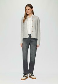 Cardigan en tricot gris avec des boutons en bois, porté sur une chemise blanche à col et un jean gris, associé à des baskets blanches et noires.