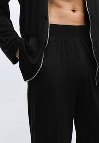 Conjunto de loungewear negro que incluye una camisa de botones con ribetes blancos y pantalones sueltos con elástico, diseñado con una textura suave y un ajuste relajado.