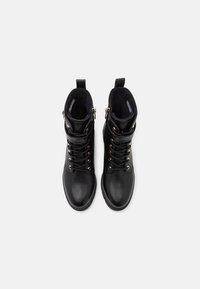 Paire de bottines en cuir noir avec laçage sur le devant, fermeture éclair latérale et col rembourré, vues de dessus sur fond blanc.
