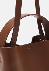 Borsa tote in pelle marrone con texture liscia, manici sottili, apertura superiore e dettagli di cucitura sottili. L'interno presenta un accent metallico.