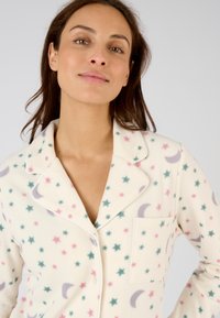Katoenen pyjama set in roomkleur met een ontwerp van pastel sterren en manen, met een zak en contrasterende bies langs de kraag en de knopenlijst.