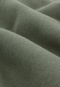 Zelená, jemne pletená tkanina s jemnou textúrou, s nenápadnými horizontálnymi pruhmi. Materiál vyzerá hladko a je mierne chĺpkovitý.