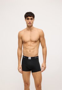 Boxeri scurți din bumbac negru, cu un brâu elastic, având un logo alb Calvin Klein, design adaptat și textură netedă.
