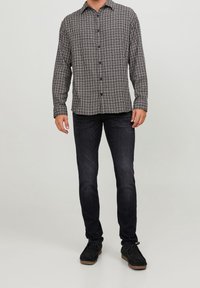 Langärmeliges kariertes Hemd in Schwarz und Weiß mit Knopfleiste, kombiniert mit dunklen schmalen Jeans und schwarzem Schuhwerk.