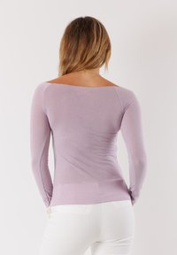 Top a maniche lunghe in lavanda chiaro, design aderente, texture liscia, con scollo ampio e maniche senza cuciture. Indossato con pantaloni bianchi.