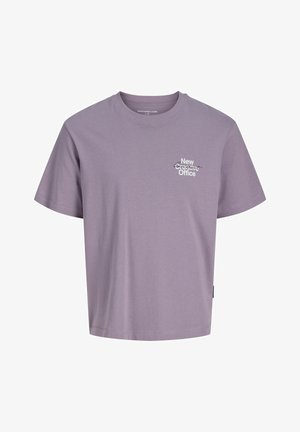 Hnedá mikina na zips s kapucňou, nosená cez svetlofialové tričko. Svetlomodré voľné rifle a čierne topánky dokončujú outfit.