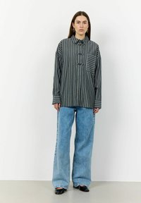 Loose-fitting, striped shirt in dark green and white, features a buttoned collar and chest pocket. Paired with wide-leg light blue jeans.