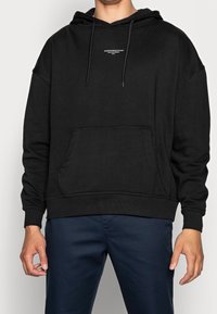 Svart hoodie i mjuk bomullsblandning, med en framficka, dragsko huva och en tryckt logotyp på bröstet. Avslappnad passform.