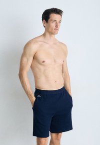 Pantalones cortos azul marino con cintura elástica y bolsillos laterales, que presentan un pequeño logotipo bordado en el lado izquierdo. Textura de tela suave.