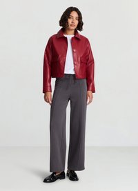Giacca corta in ecopelle rossa con due tasche frontali, t-shirt bianca e pantaloni grigi a gamba larga, completati da scarpe nere.