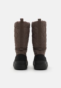 Botas acolchadas marrones con parte superior acolchada, acentos de ante negro y una suela de goma negra gruesa, que cuentan con una pestaña de tirón y correas decorativas.
