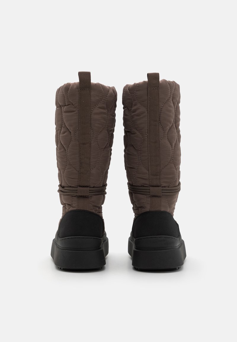 Brązowe pikowane buty z ocieplanym wierzchem, czarnymi zamszowymi akcentami oraz grubą czarną gumową podeszwą, z pętelką do wsuwania i dekoracyjnymi paskami.