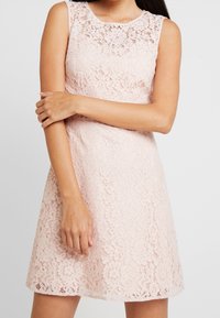 Lace dress in light pink, sleeveless design with a round neckline. Features intricate floral patterns and a flared silhouette.