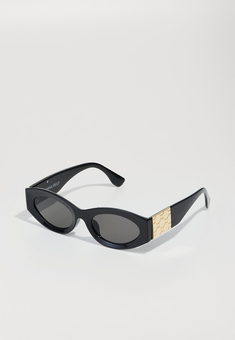 Black sunglasses with oval lenses, a sleek frame, and a textured gold accent on the sides. The design features smooth curves and a glossy finish.