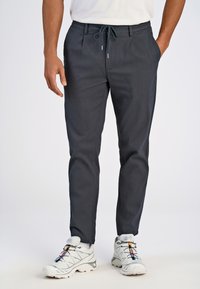 Pantalons légers gris foncé avec une taille à cordon, jambe fuselée, poches avant et texture lisse, associés à des chaussures de sport blanches.