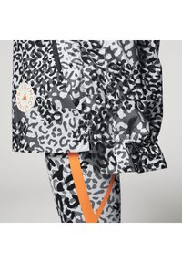 Leopardmönstrad jacka i grå nyanser, med en logopatch och elastiska manschetter, tillsammans med matchande leggings som har orangea ränder.