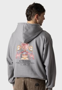 Sudadera gris con un estampado gráfico colorido en la parte posterior que presenta animales y texto. Hecha de material suave, diseñada para la comodidad y el uso casual.