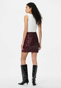 Top blanco sin mangas combinado con una falda corta de lentejuelas burdeos. El conjunto se complementa con botas negras hasta la rodilla de punta afilada.