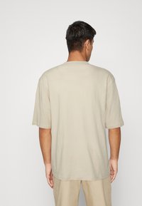 Beige bavlněné tričko s krátkým rukávem a kulatým výstřihem, které má pohodlný střih a hladkou texturu. Zobrazeno ze zadní strany.