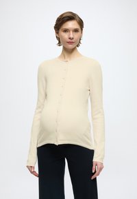 Light beige cardigan made of soft material, featuring a round neck, long sleeves, and a front button closure. Accentuated with a curved hem.