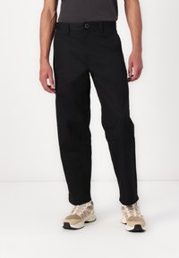 Black trousers made of lightweight fabric, featuring a straight-leg design, button closure, and side pockets, paired with beige athletic shoes.