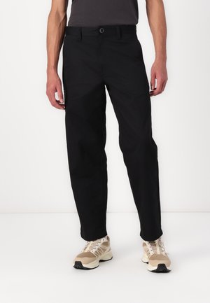 Black trousers made of lightweight fabric, featuring a straight-leg design, button closure, and side pockets, paired with beige athletic shoes.