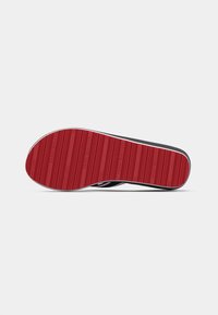 Black shoe with a red rubber outsole featuring horizontal grooves for traction. Reinforced sides and white stitching along the edges.