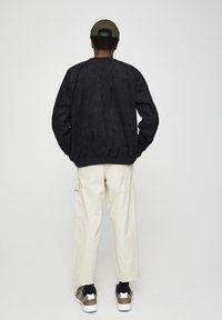 Sort ruskindsbomberjakke med ribbet kant, kombineret med cremefarvede cargobukser. Outfit fuldendes med brune og hvide sneakers.