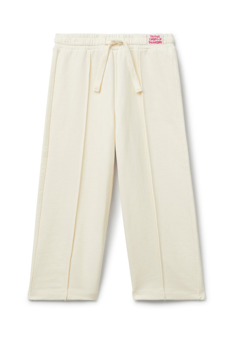Krémové kalhoty s širokými nohavicemi, elastickým pasem a stahovací šňůrkou, se svislými švy a malou červenou nášivkou na pase.