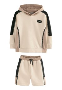 Beige hættetrøje og matchende shorts med sorte sidepaneler, snøre i taljen og logo på brystet. Blødt, tekstureret stof.