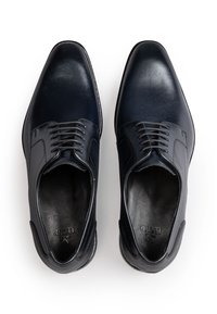 Een paar gepolijste zwarte leren herenschoenen met gesloten vetersluiting, gezien van boven op een witte achtergrond.